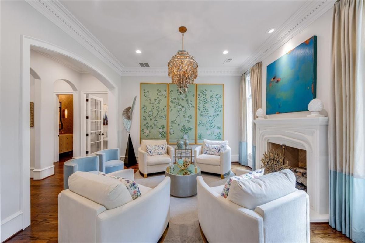 A living room with paintings, a chandelier, a fireplace, chairs, and a coffee table.