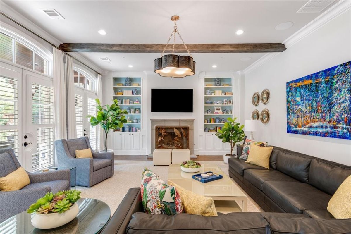 A living room with windows, an exposed beam ceiling, a TV, a fireplace, shelves, a couch, chairs, and a coffee table.