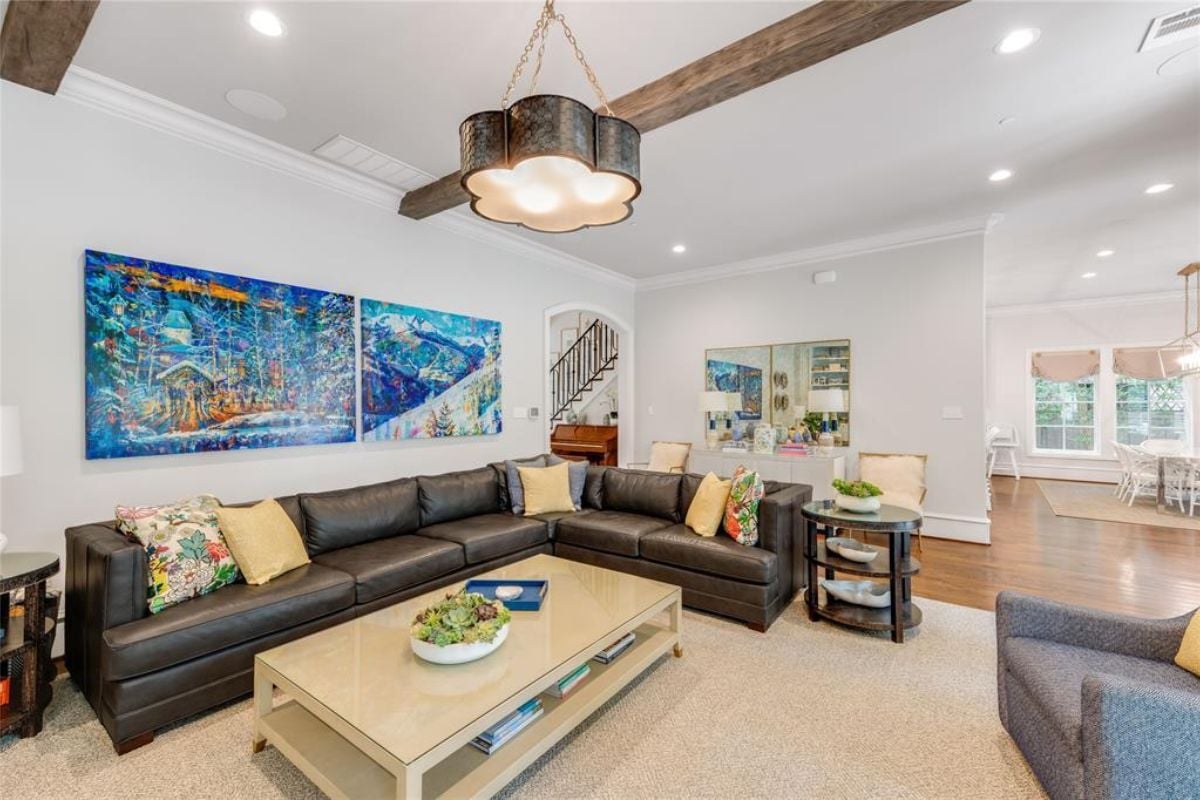 A living room with a chandelier, an exposed beam ceiling, a TV, a fireplace, a chair, and a coffee table.