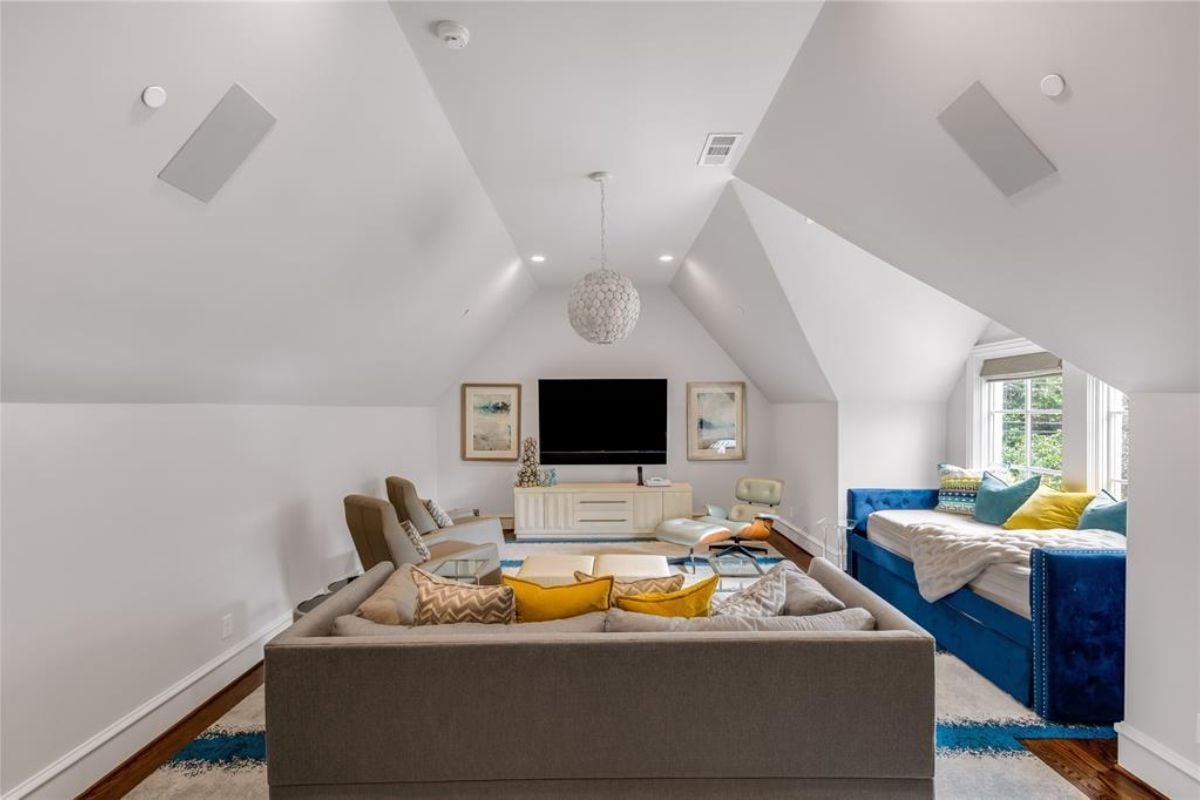 A family room with a vaulted ceiling, a window, a chandelier, couches, a TV, and a painting.