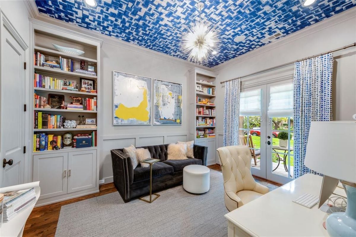 A home office with a cabinet, a painted ceiling, a chandelier, shelves, additional cabinets, a couch, a chair, and a desk.