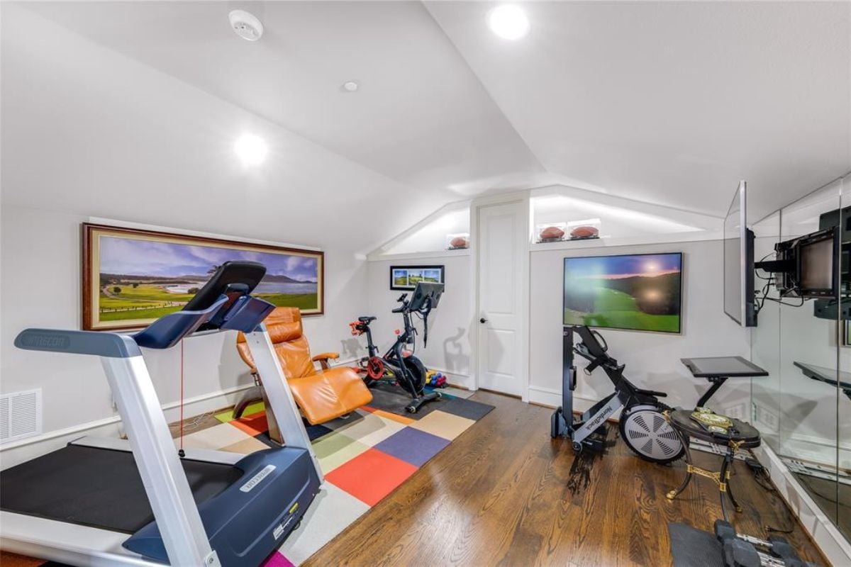 A home gym with paintings, a TV, a chair, a rug, and gym equipment.