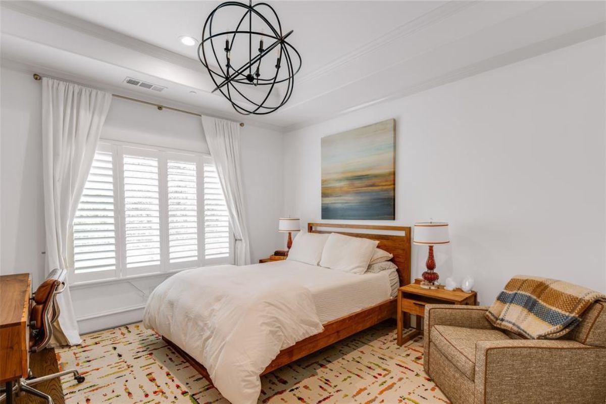 A bedroom with a bed, a window, a painting, a nightstand, a single couch, and a desk with a chair.
