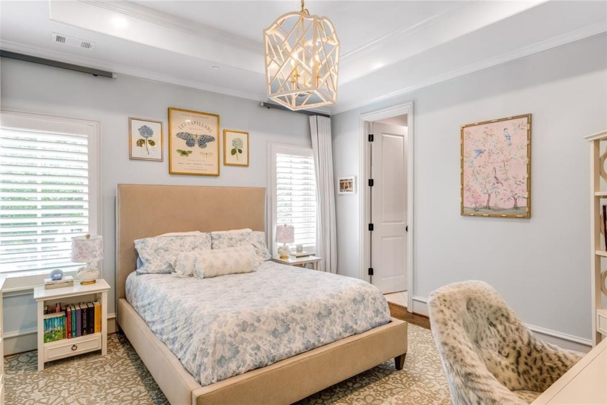 A bedroom with a chandelier, windows, nightstands, a painting, and a bed.