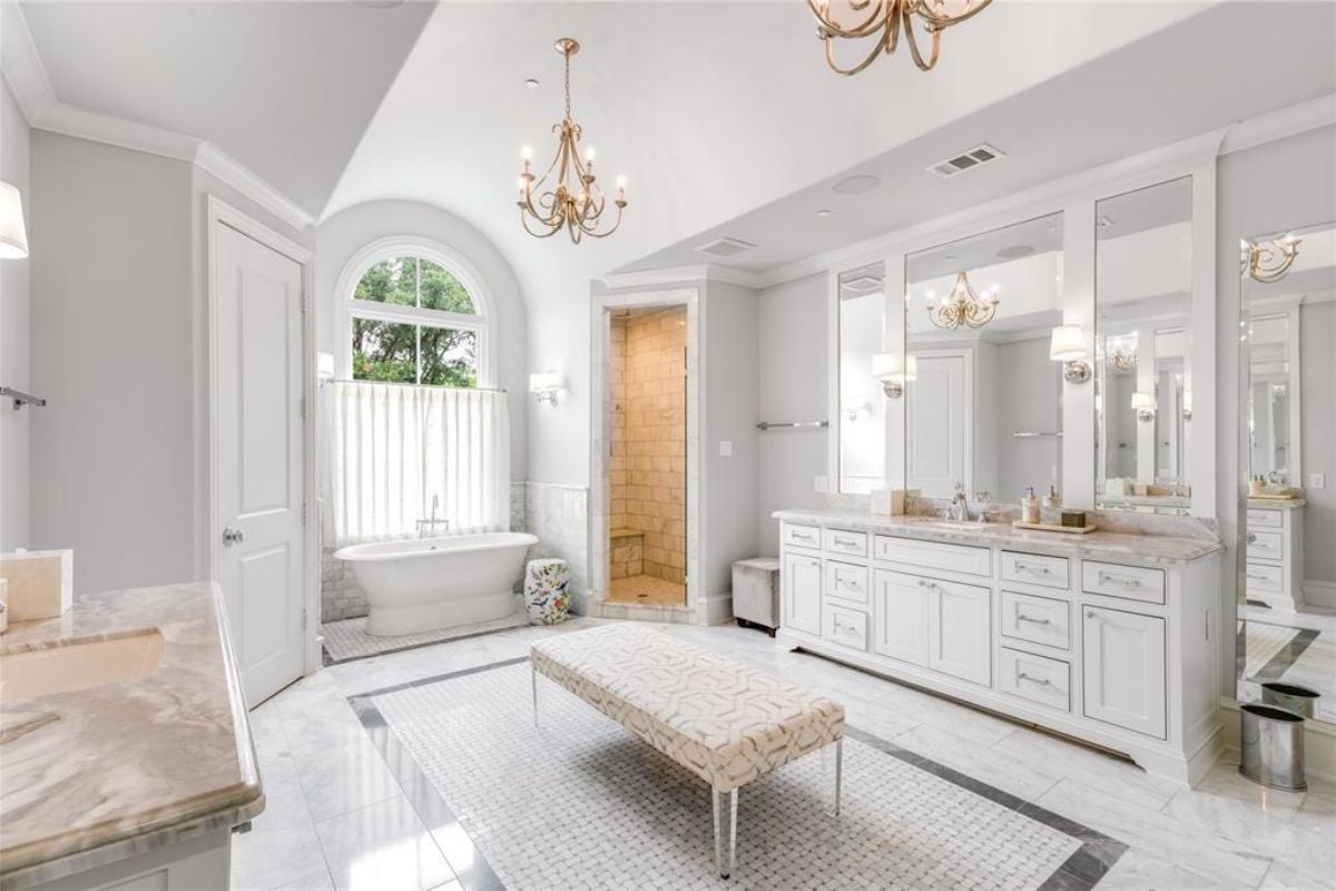 A bathroom with a vanity, mirrors, a cabinet, a bench, a window, and a bathtub.