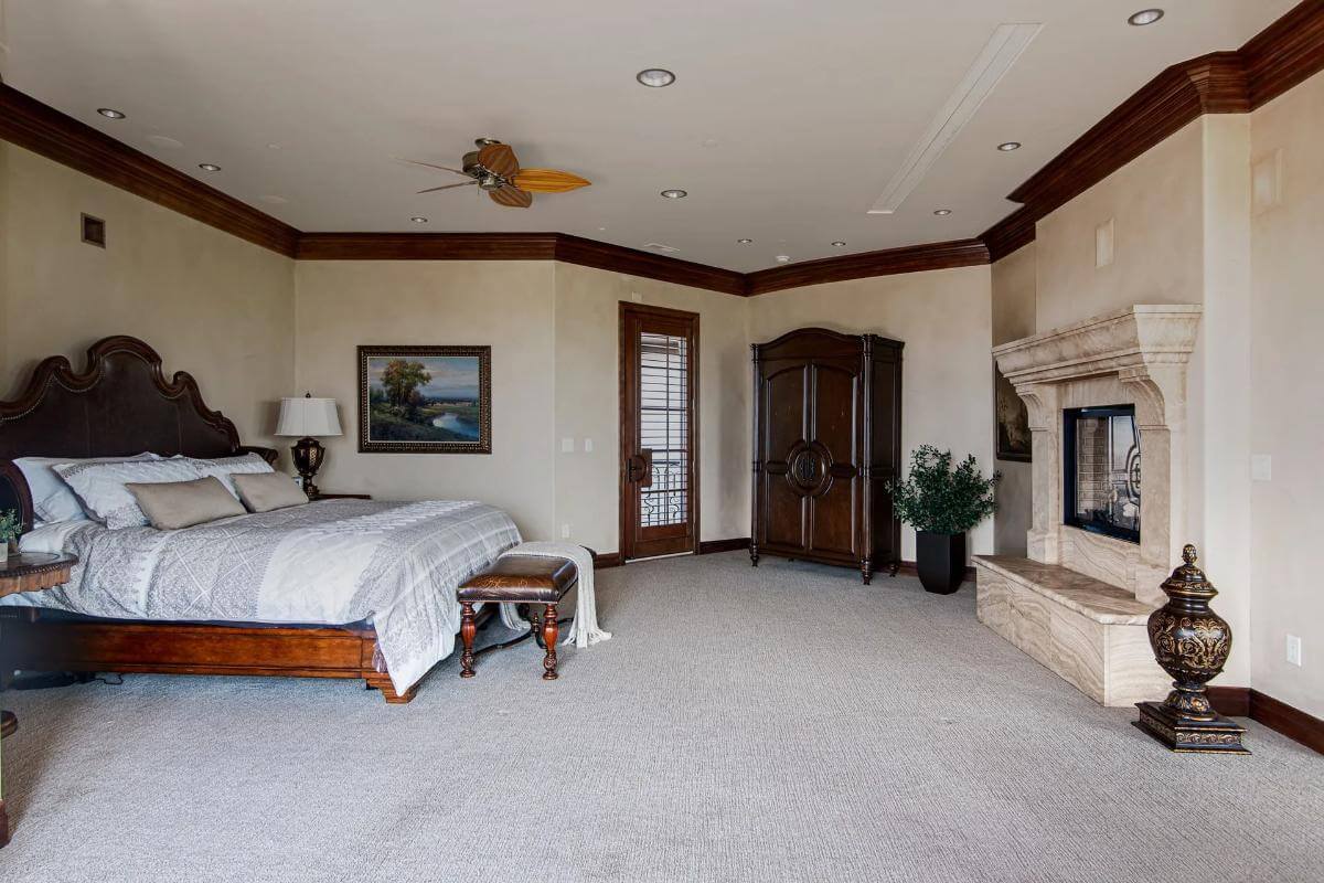 Primary bedroom with a fireplace and a dark wood bed over the carpeted floor.