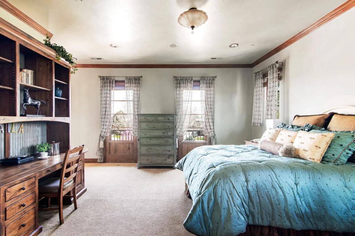 Bedroom with a wooden desk and framed windows dressed in sheer curtains.