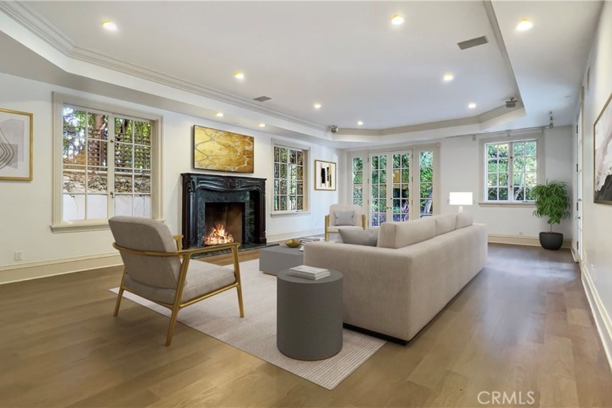 A living room with windows, chairs, paintings, a fireplace, a rug, couches, and a coffee table.