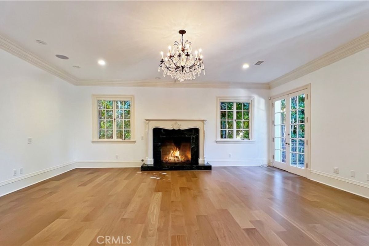 An empty room with a fireplace, windows, and a chandelier.