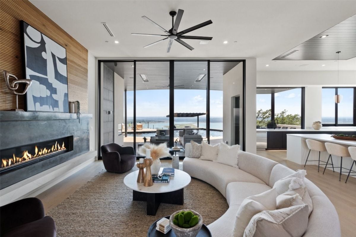 A living room with a ceiling fan, fireplace, painting, chairs, a curved white couch, and a round center table.