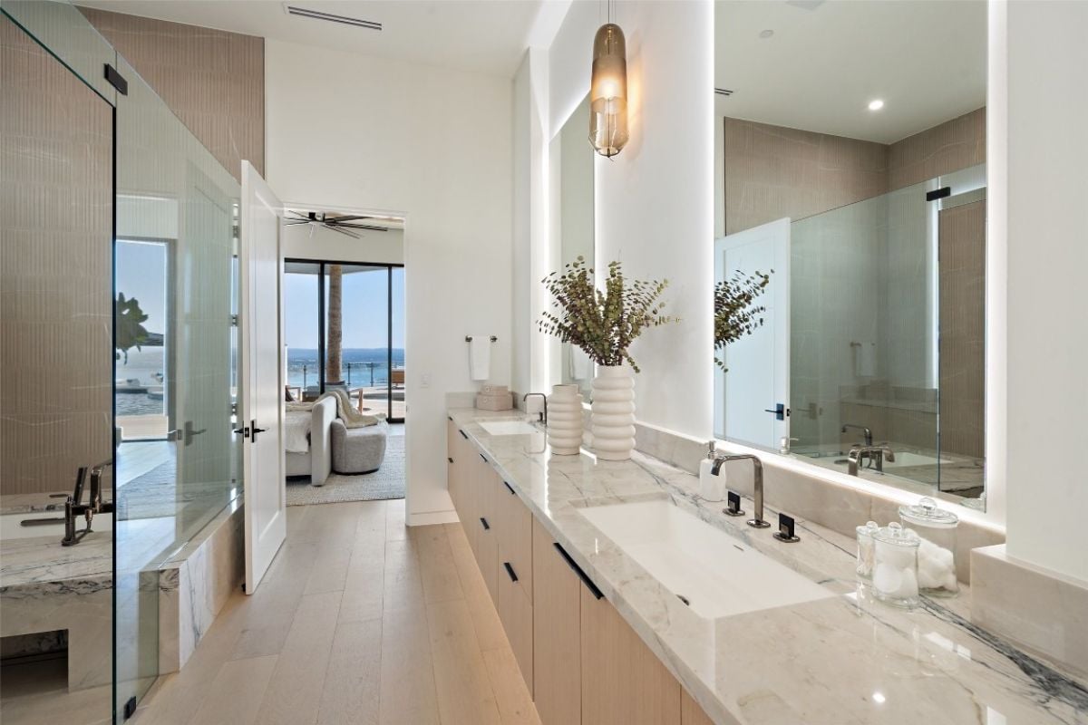 A bathroom with dual vanities, a mirror, a cabinet, and a shower room.