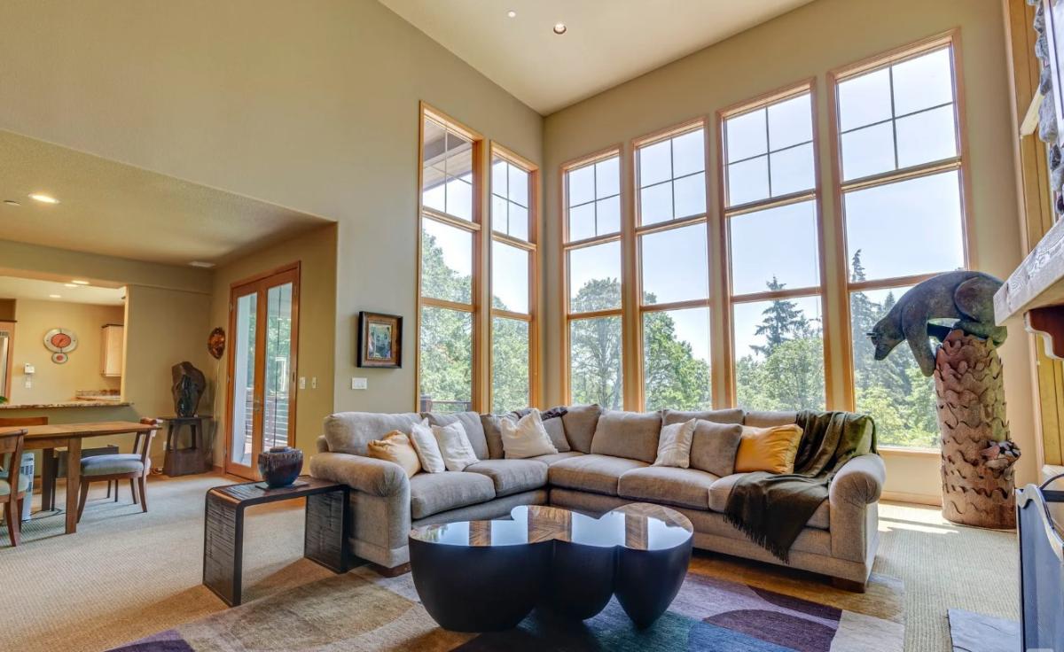 Living room with high ceilings, couches and large glass windows.