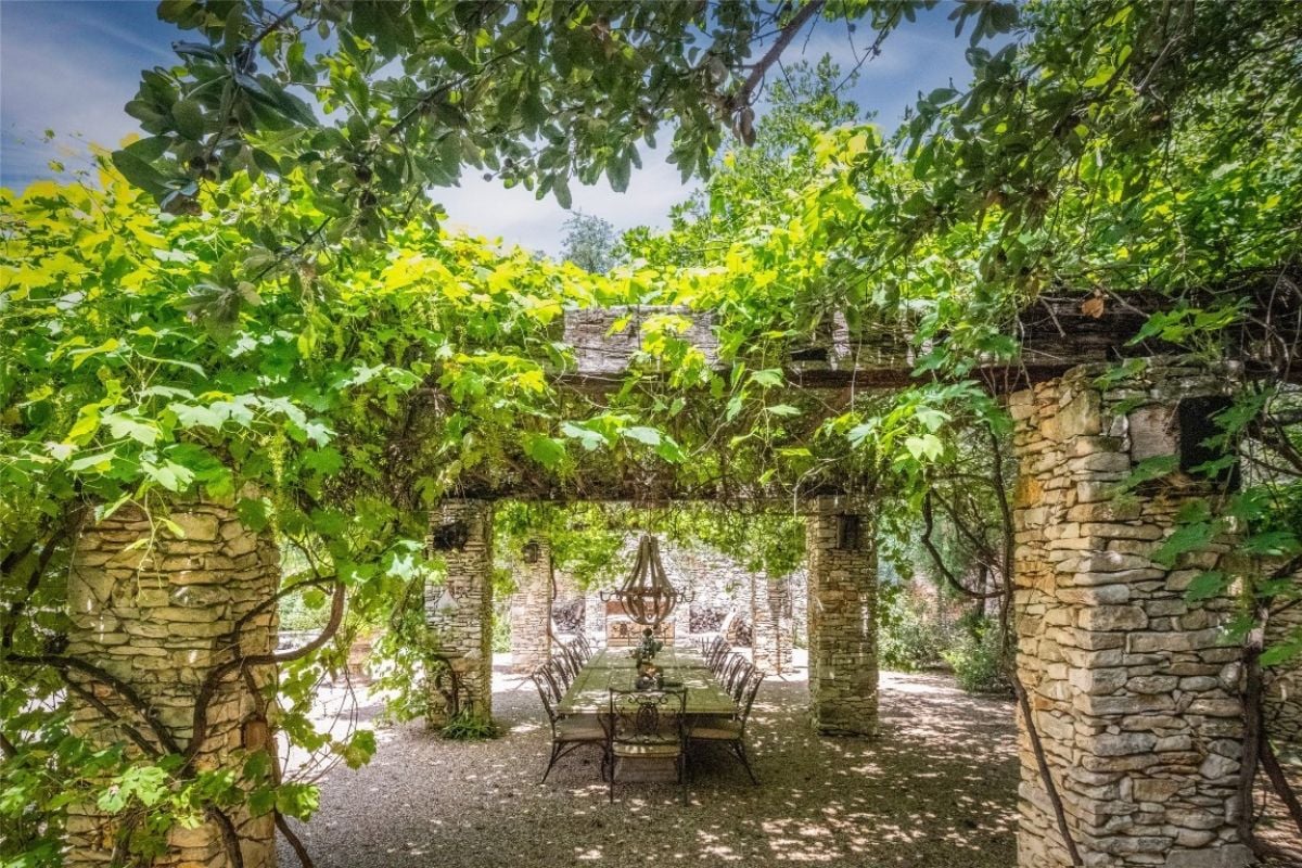 A patio with stone columns, plants, and a dining table surrounded by chairs.