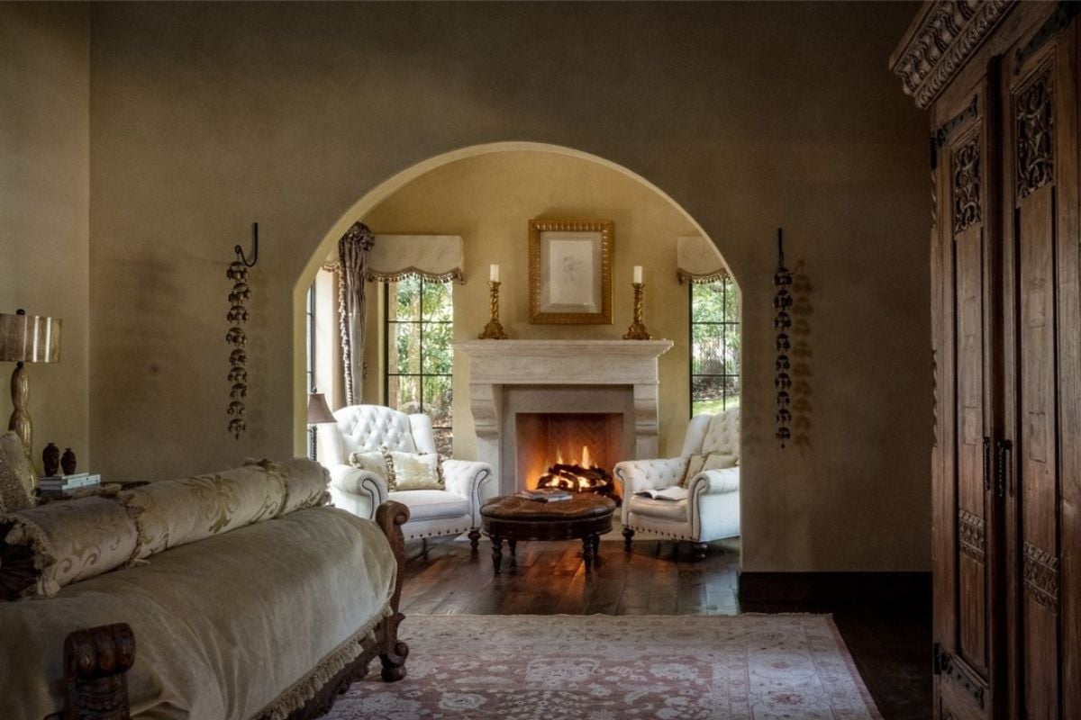 A bedroom with a bed, rug, fireplace, single couches, and a round center table.
