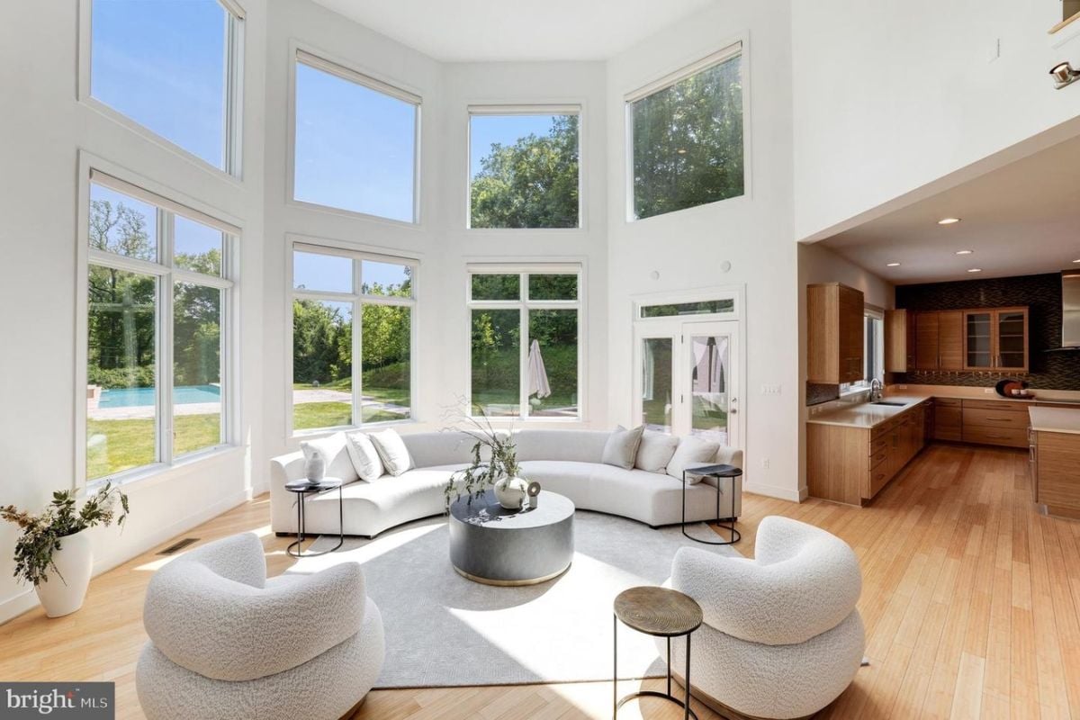 A living room with a high ceiling, windows, a curved couch, chairs, a rug, and a coffee table.