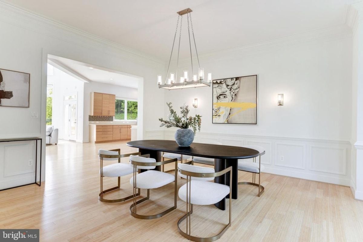 A dining room with a chandelier and a table with a vase on top, surrounded by chairs.