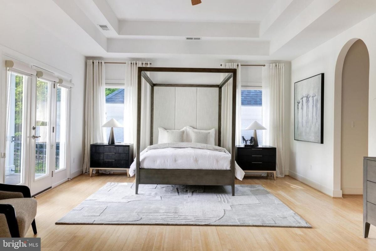 A bedroom with a canopy bed, windows, a painting, a rug, and nightstands.
