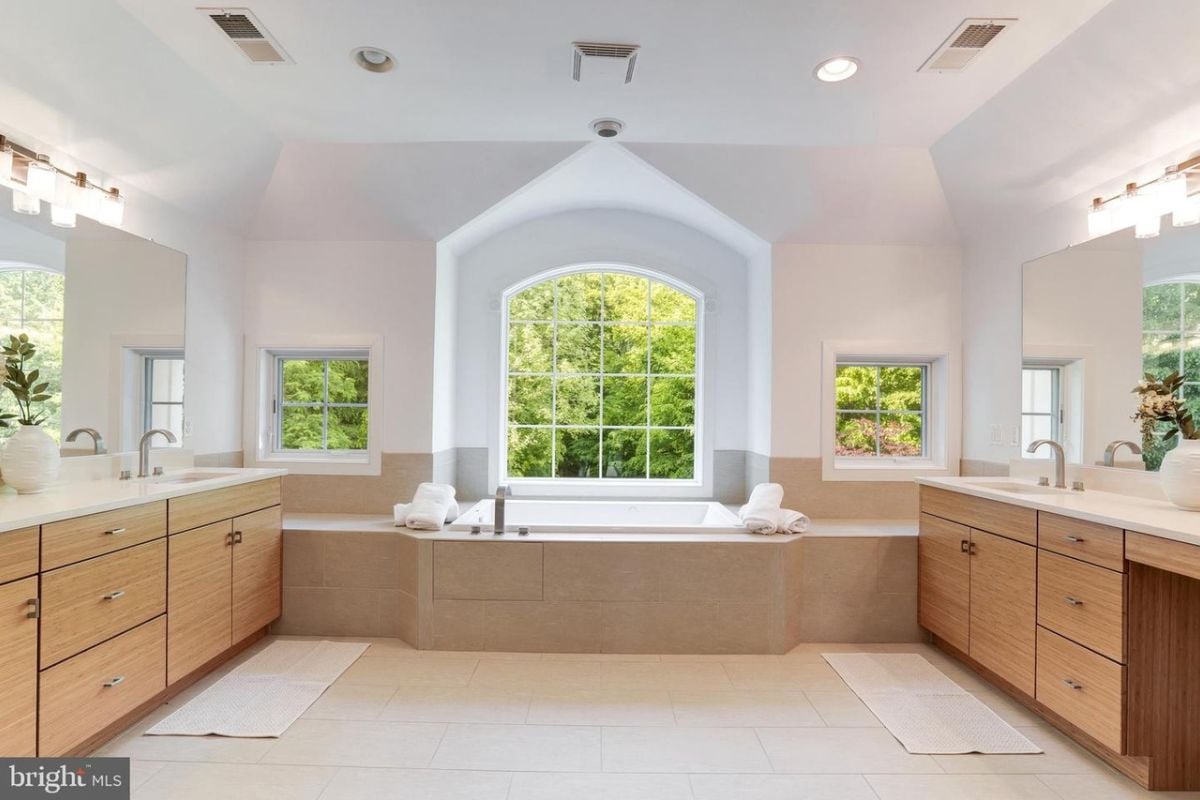 A bathroom with windows, vanities, a sink, and a bathtub.