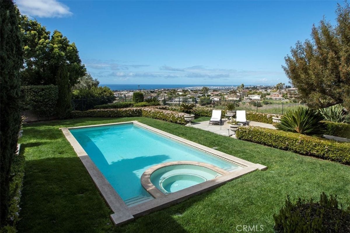 A swimming pool with a jacuzzi, surrounded by plants.