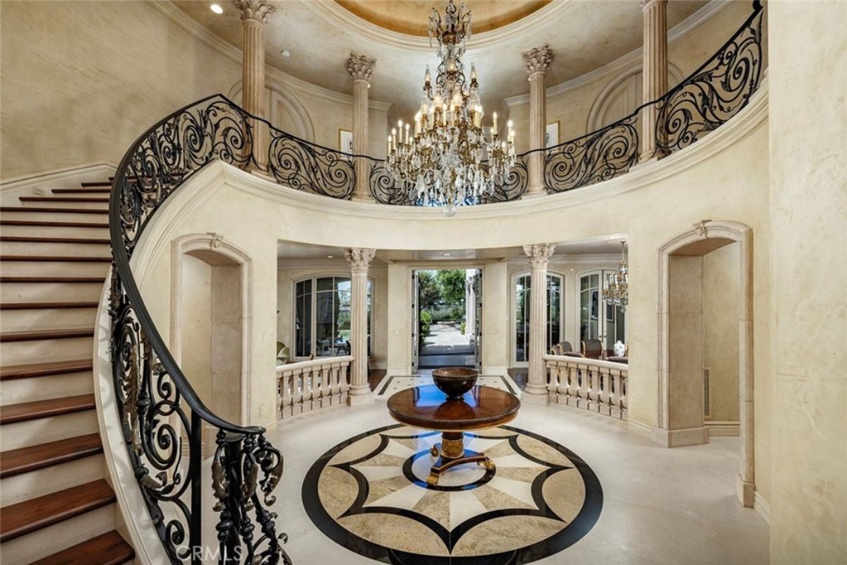 A foyer with a tiled floor, a round center table, a chandelier, and a staircase.