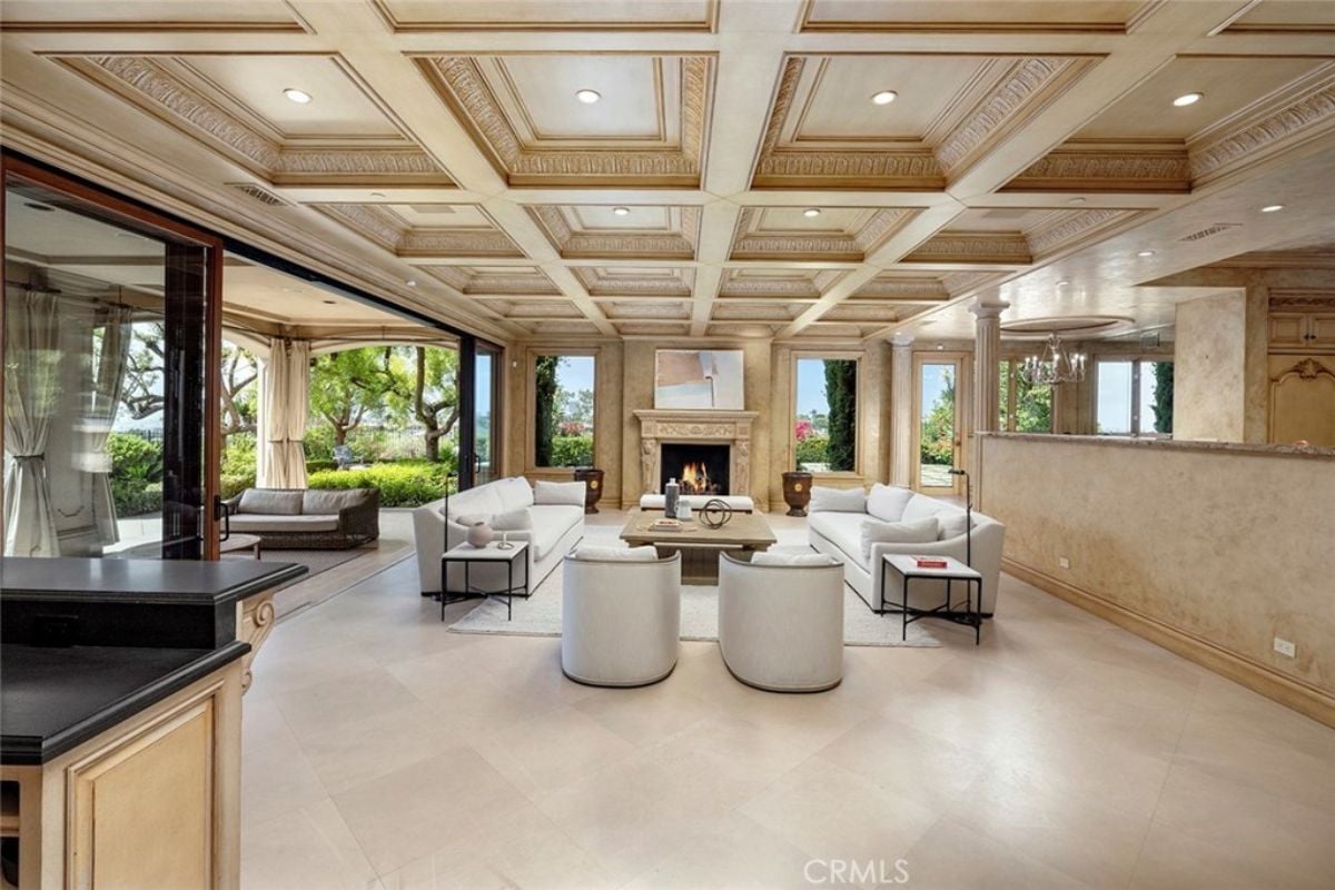 A living room with a ceiling with molding, a fireplace, a painting, windows, a rug, white couches, chairs, and a center table.