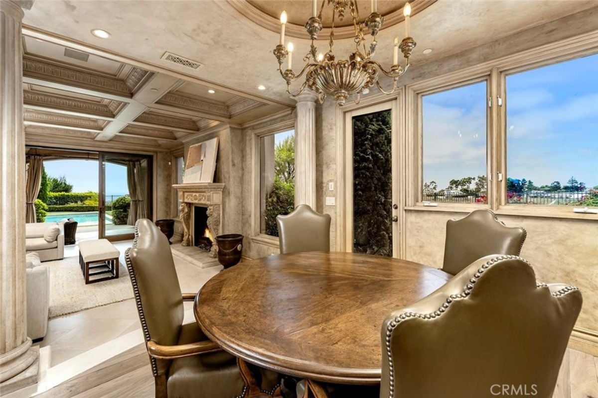 A dining room with a chandelier, windows, and a round table surrounded by chairs.