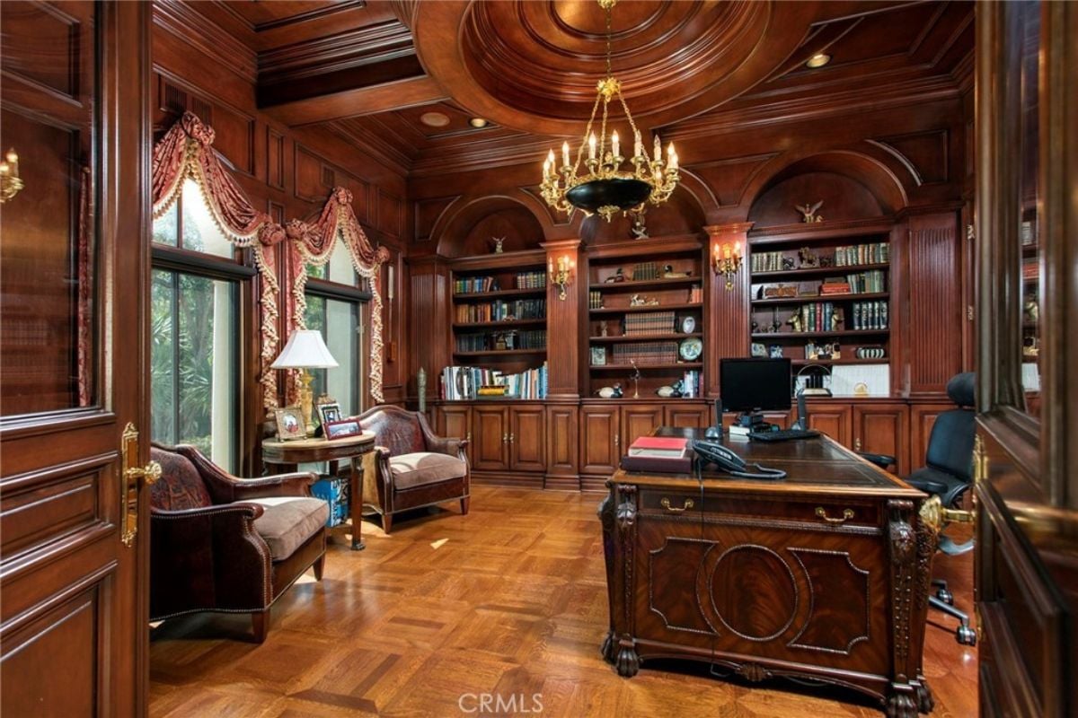 A home office with shelves, cabinets, single couches, a chandelier, and a desk with office chairs.