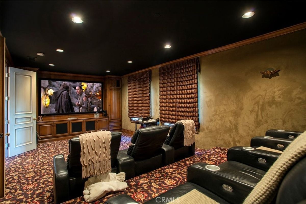 A home theater with a floral floor, a large screen, a black ceiling, and cinema chairs.