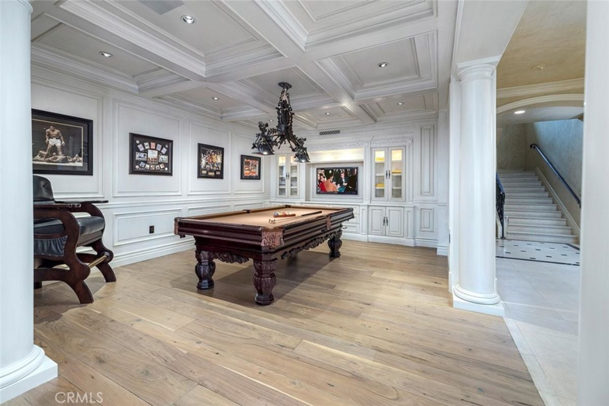 A game room with a ceiling with molding, paintings, a TV, and a pool table.