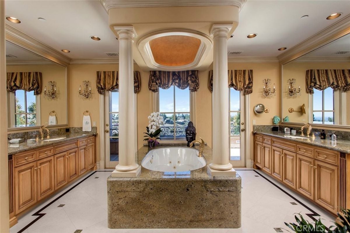 A bathroom with vanities, cabinets, windows, mirrors, and a bathtub.