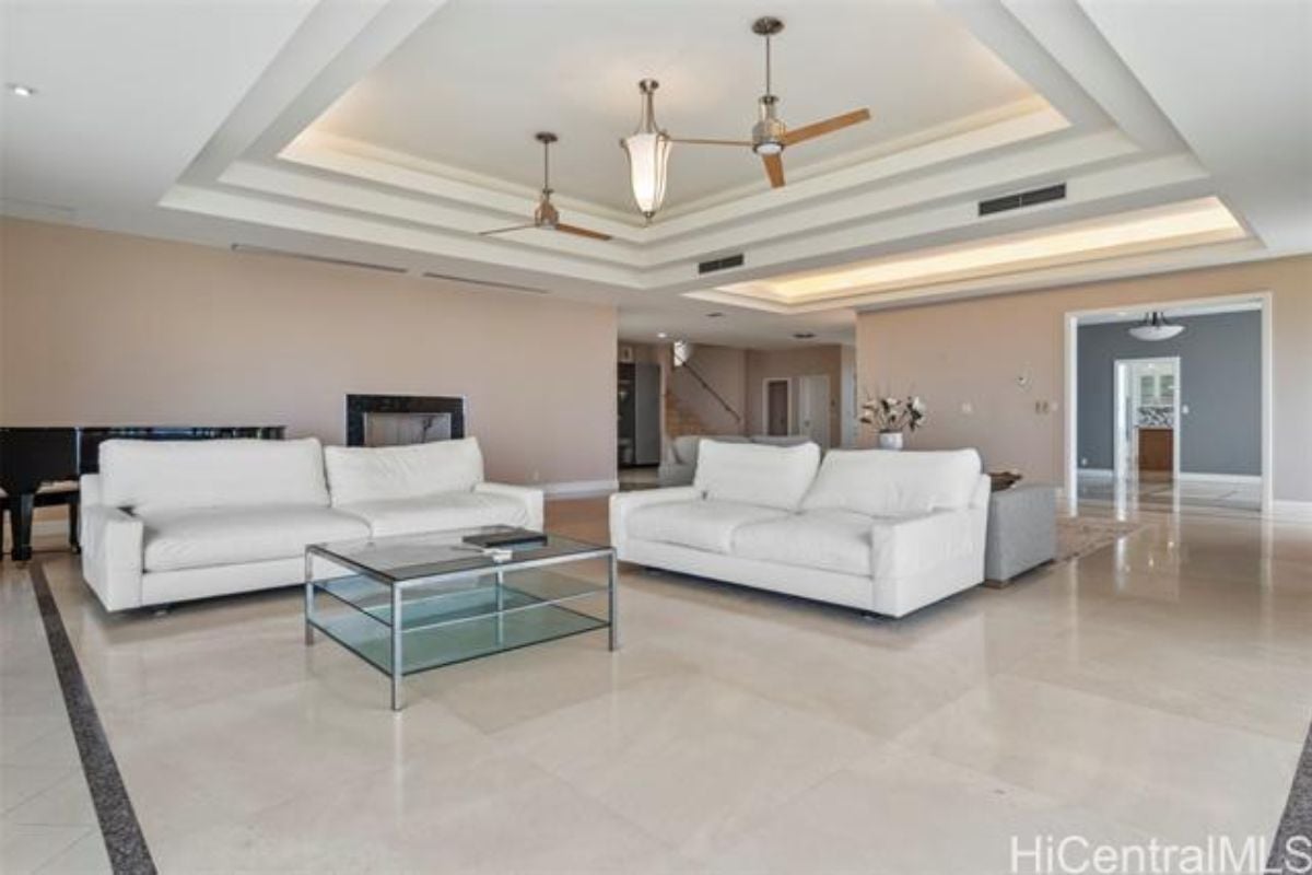 A living room with ceiling fans, tiled floor, couches, and a center table.