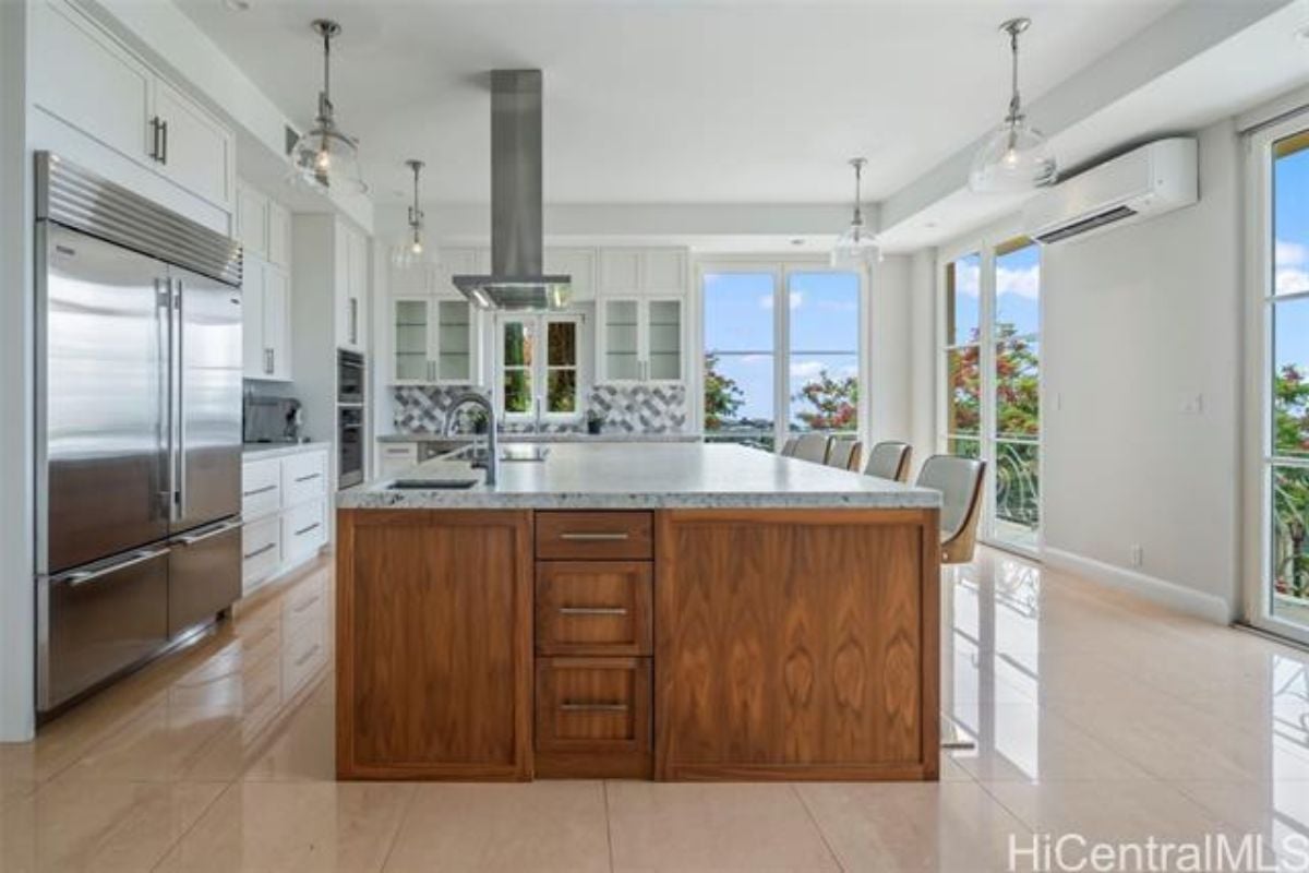 A kitchen with an island, sink, chairs, countertops, and kitchen appliances.