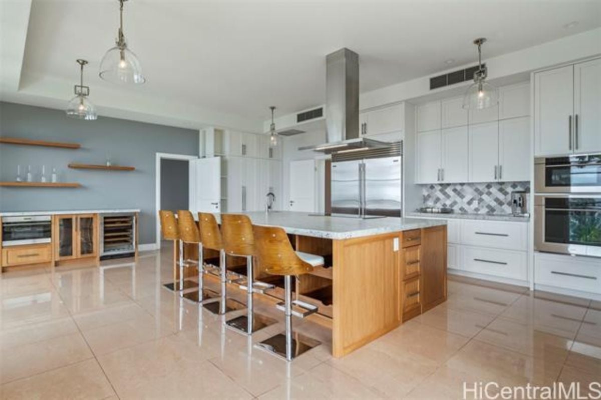 A kitchen with an island, sink, chairs, countertops, and kitchen appliances.
