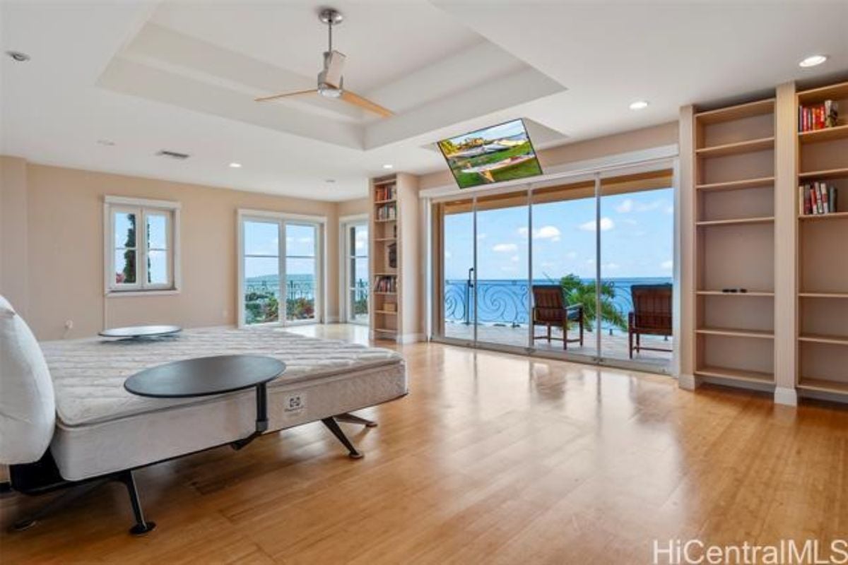 A bedroom with a bed, ceiling fan, shelves, TV, and a glass sliding door leading to the balcony.