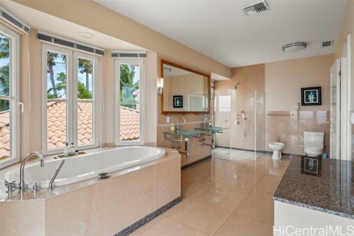 A bathroom with glass vanities, windows, a bathtub, and a toilet.