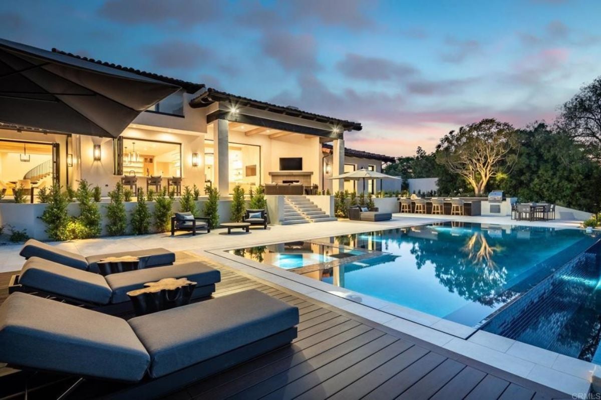 A swimming pool with an umbrella and comfy chairs.