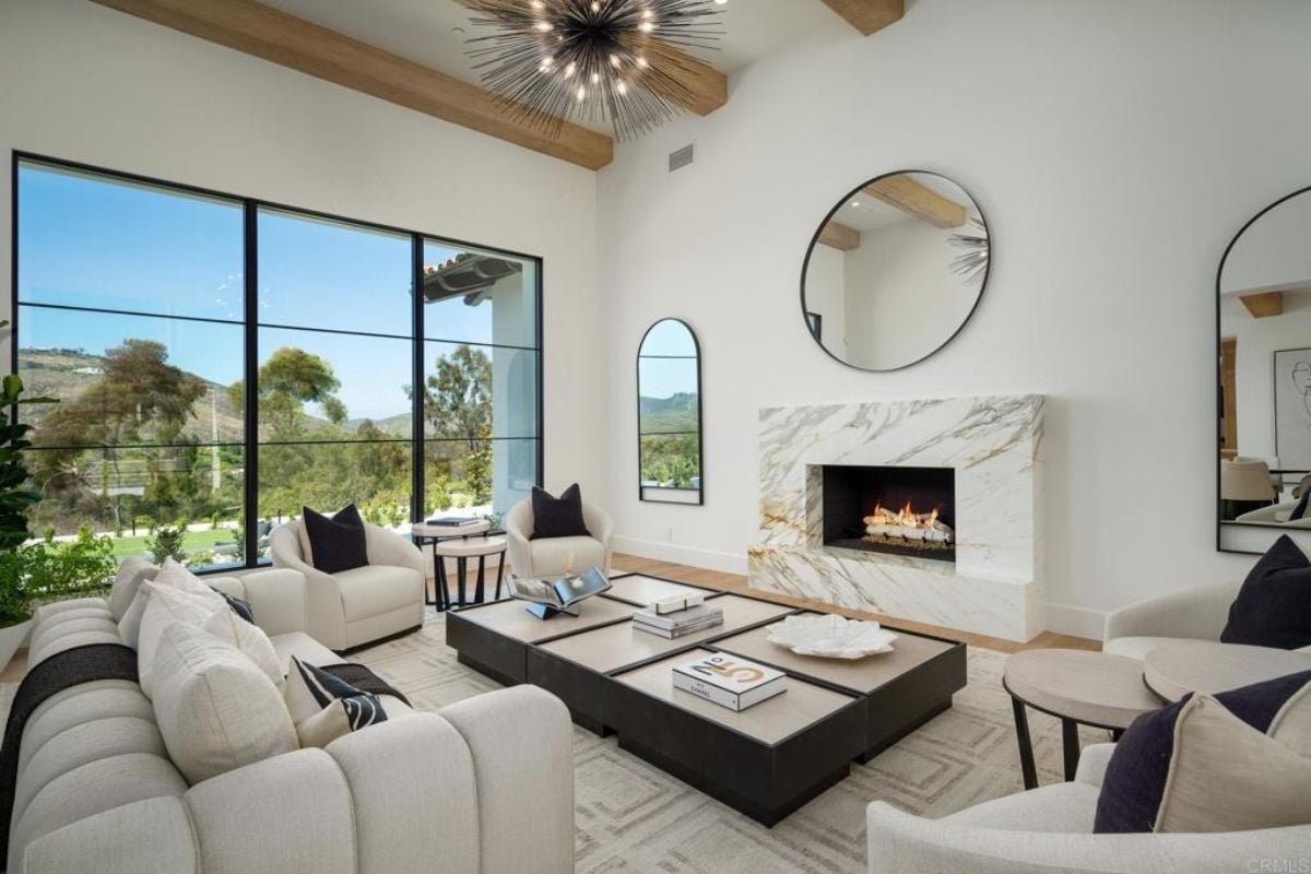 A living room with a window, a mirror, a fireplace, a couch, chairs, and a center table.