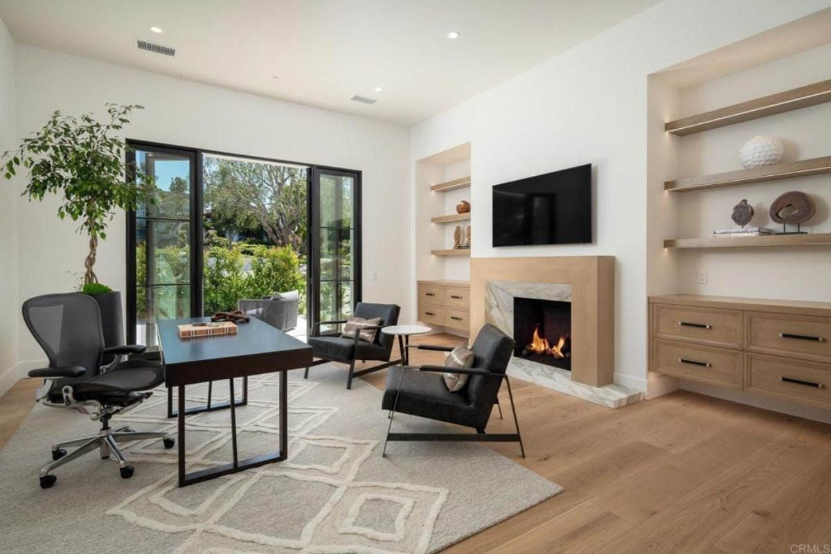 A home office with a TV, shelves, cabinets, a fireplace, a rug, chairs, and a desk with an office chair.