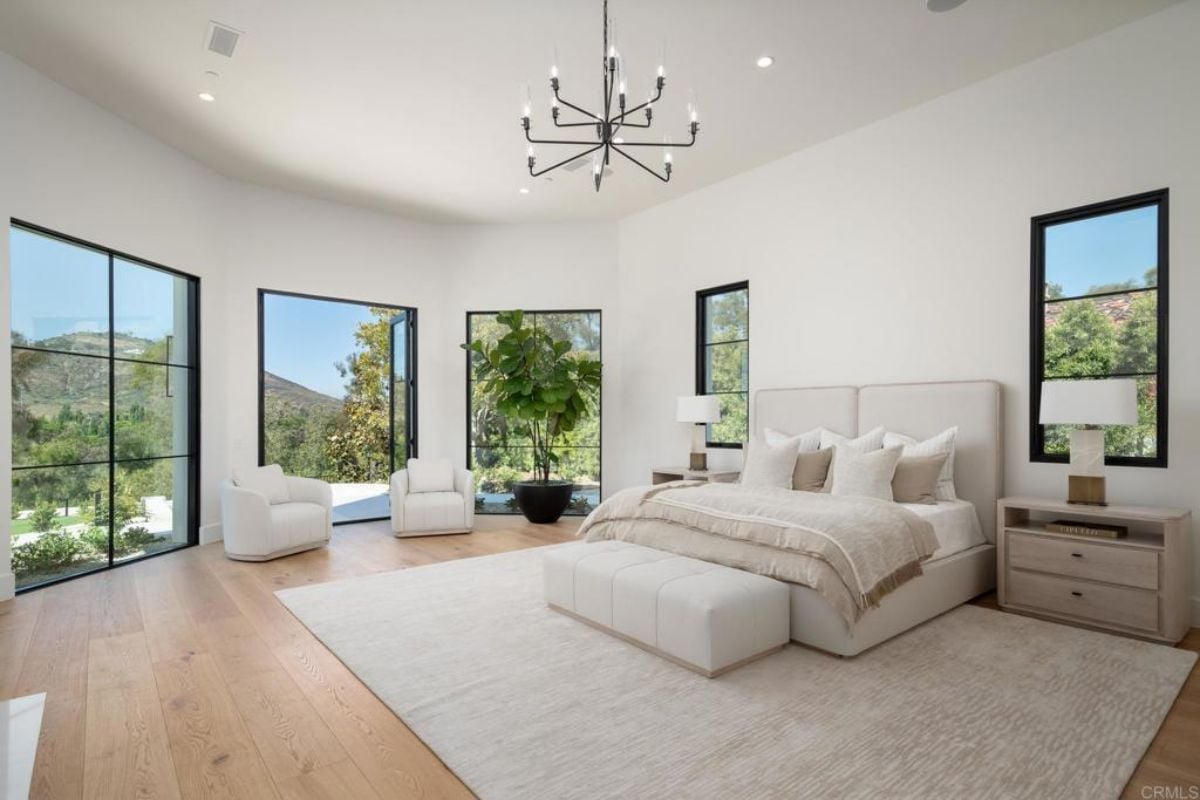 A bedroom with a bed, windows, a rug, a nightstand, and a chandelier.