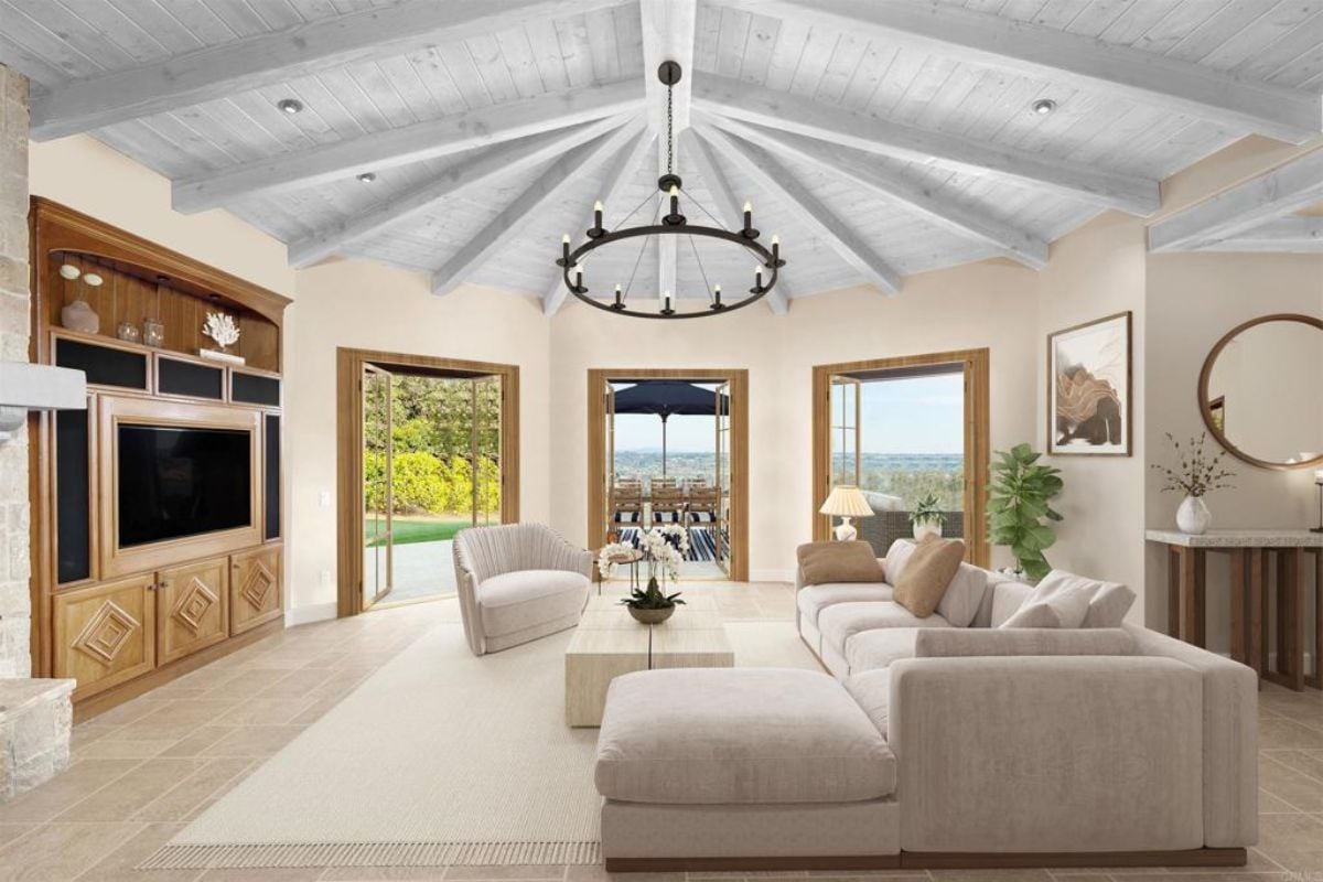 A living room with an exposed beam ceiling, a chandelier, a TV, a couch, a rug, and a coffee table.