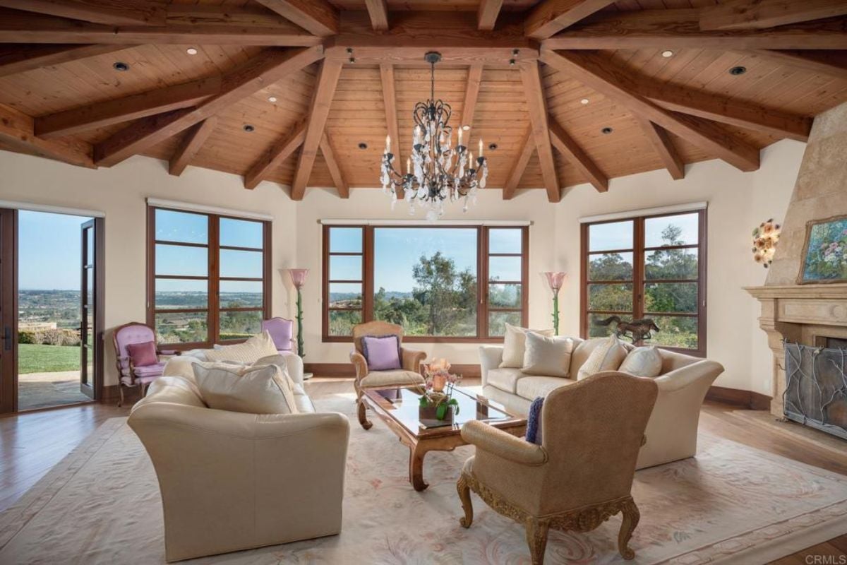 A living room with an exposed beam ceiling, a chandelier, a windows, fireplace, a couch, a rug, and a coffee table