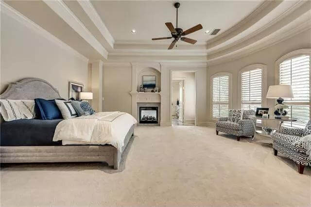 Primary bedroom with a step ceiling, a fireplace, and a sitting area by the louvered windows.