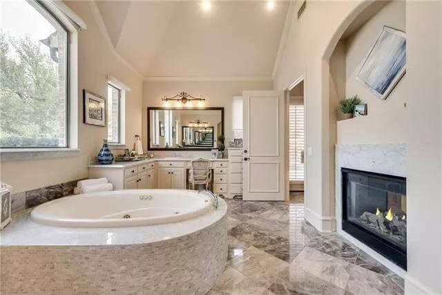 Primary bathroom with an L-shaped vanity, a whirlpool tub, and a double-sided fireplace.