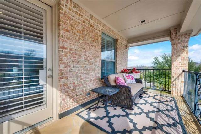 Balcony with brick pillars and a wicker sofa over the patterned area rug.
