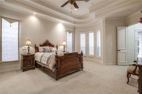 Primary bedroom with a step ceiling, a bow window, and a wooden bed over the carpeted floor.
