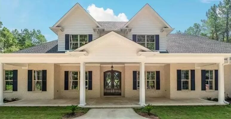 Front view with shuttered windows and an expansive entry porch topped by twin dormers.