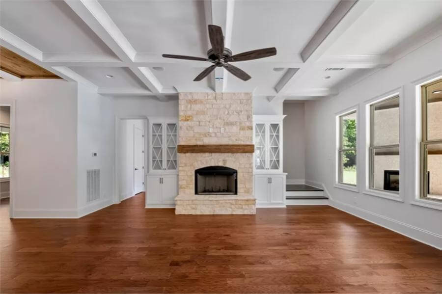Family room with a coffered ceiling and a stone fireplace flanked by white built-ins.