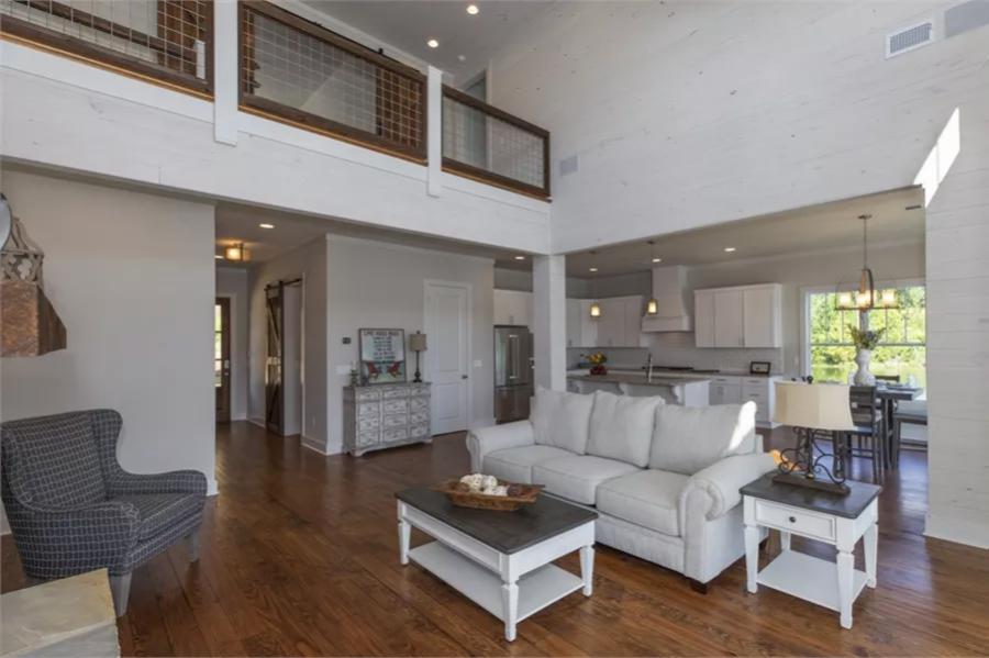 The living room includes white tables, a wingback chair, and a view of the balcony.