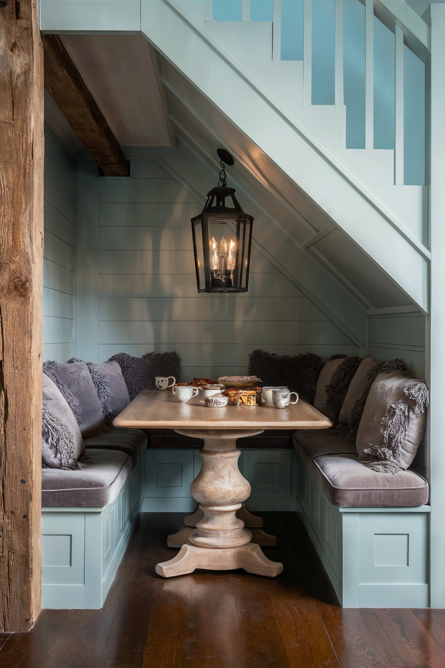 An under-the-stairs breakfast nook with light blue paneled walls, a wooden table, and cushioned bench seating