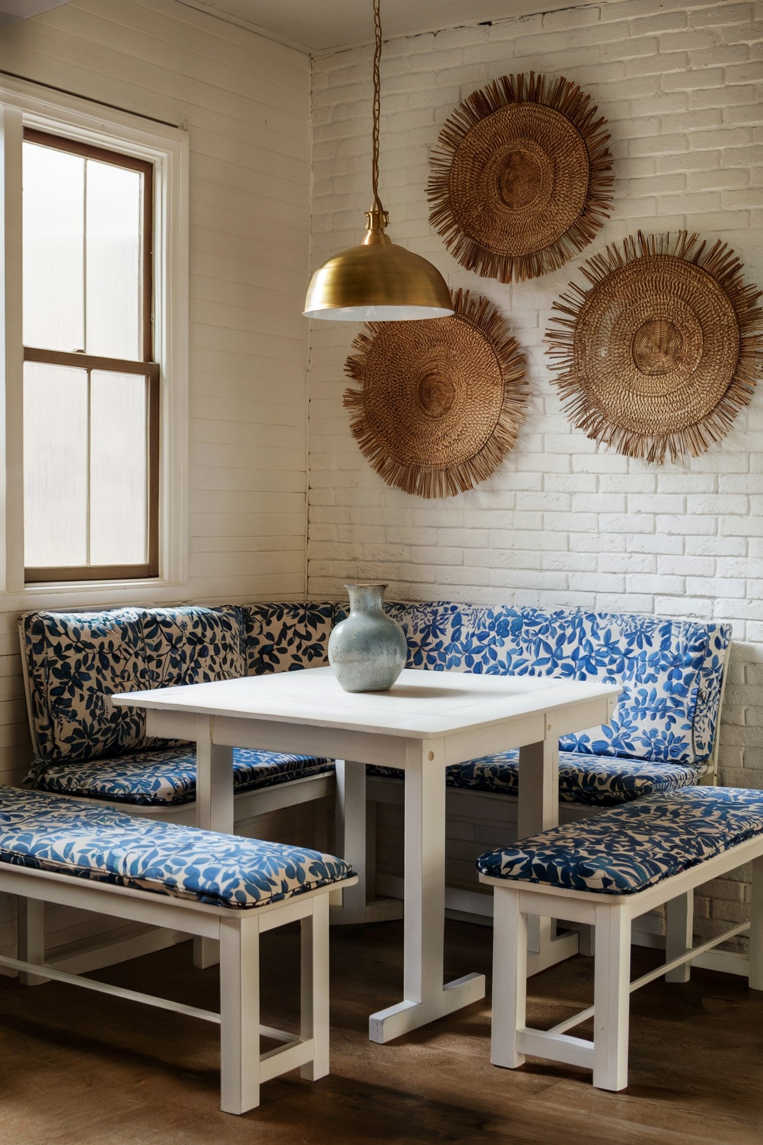 Small nook with blue patterned cushions, a white table, and gold pendant light